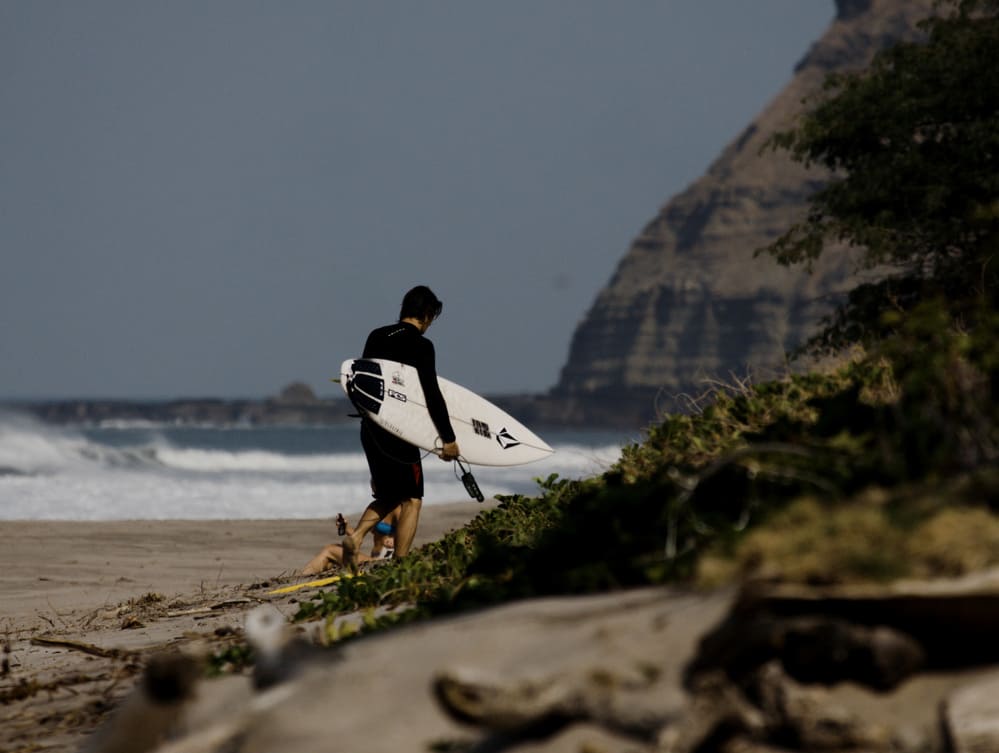 man walking down beach with surfboard