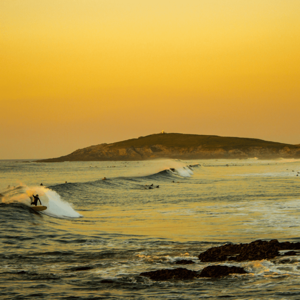 surfers surfing wave at fistral beach during sunset