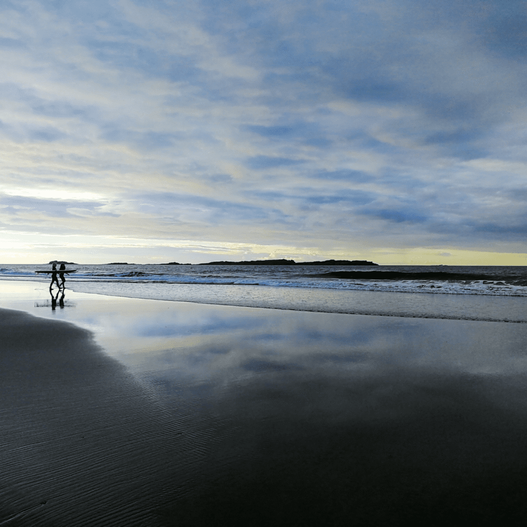 two people walking down to the sea with their surfboards during sunrise